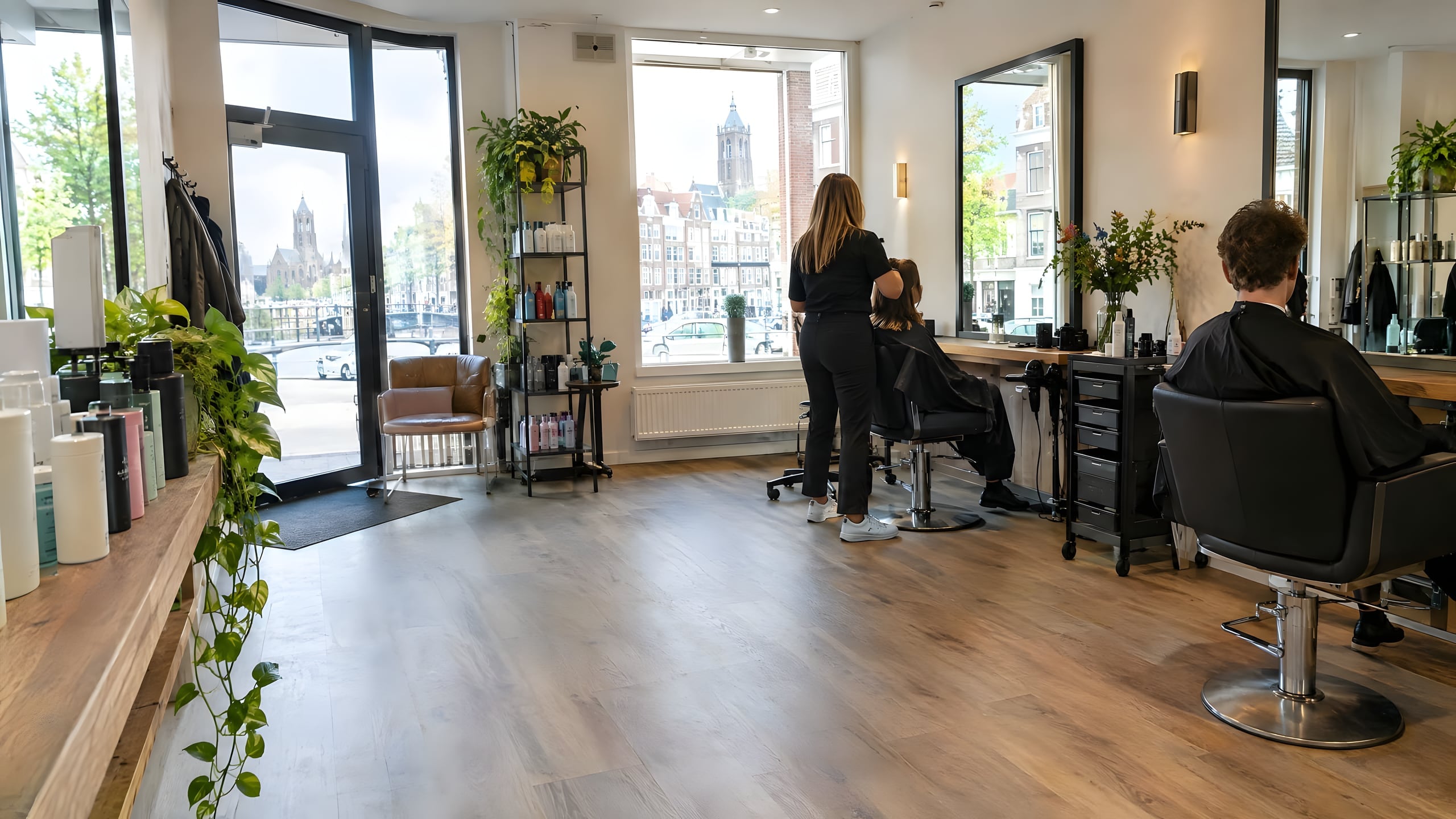 Kapsalon met grote ramen en daglicht, stylisten aan het werk bij de stoelen.